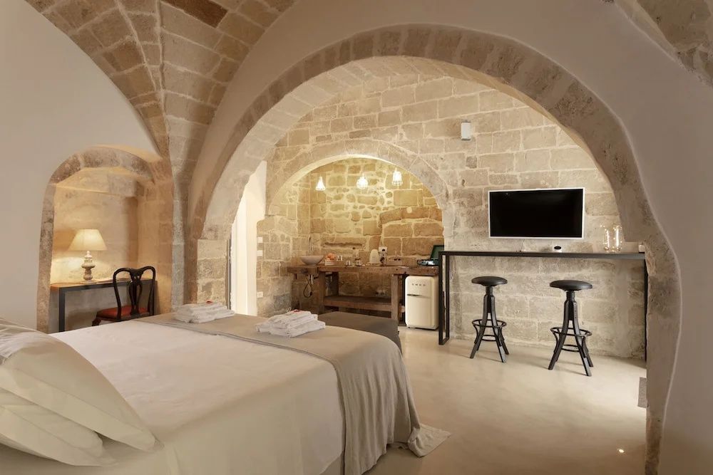 Hotelzimmer unter einem historischen Steinrundbogen mit Doppelbett, Fernseher und Sitzgelegenheiten.