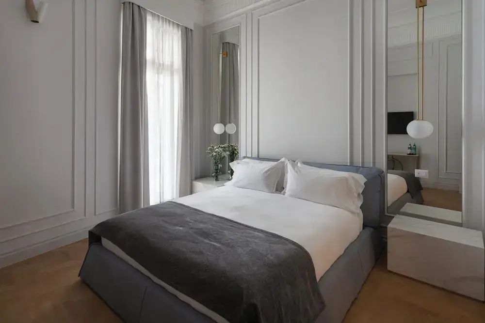 Doppelbett mit weißer Bettwäsche und grauer Decke in einem hell gestalteten Hotelzimmer.