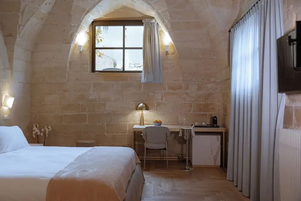 Hotelzimmer mit gewölbten Natursteinwänden, Schreibtisch und Fenster.