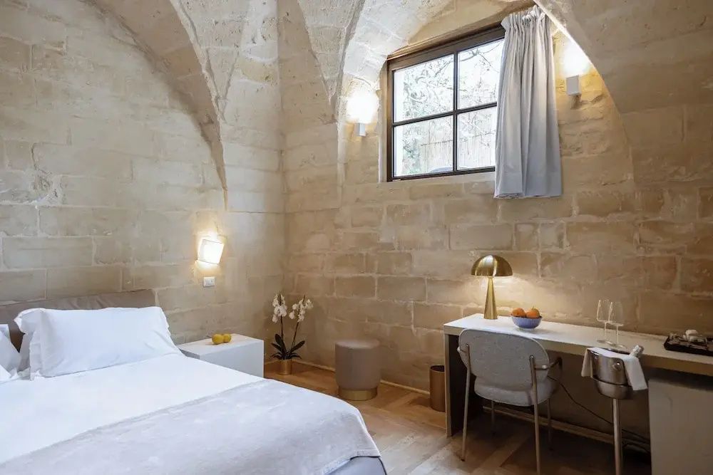 Helles Hotelzimmer mit Natursteingewölbe, Bett, Schreibtisch und Lampen.