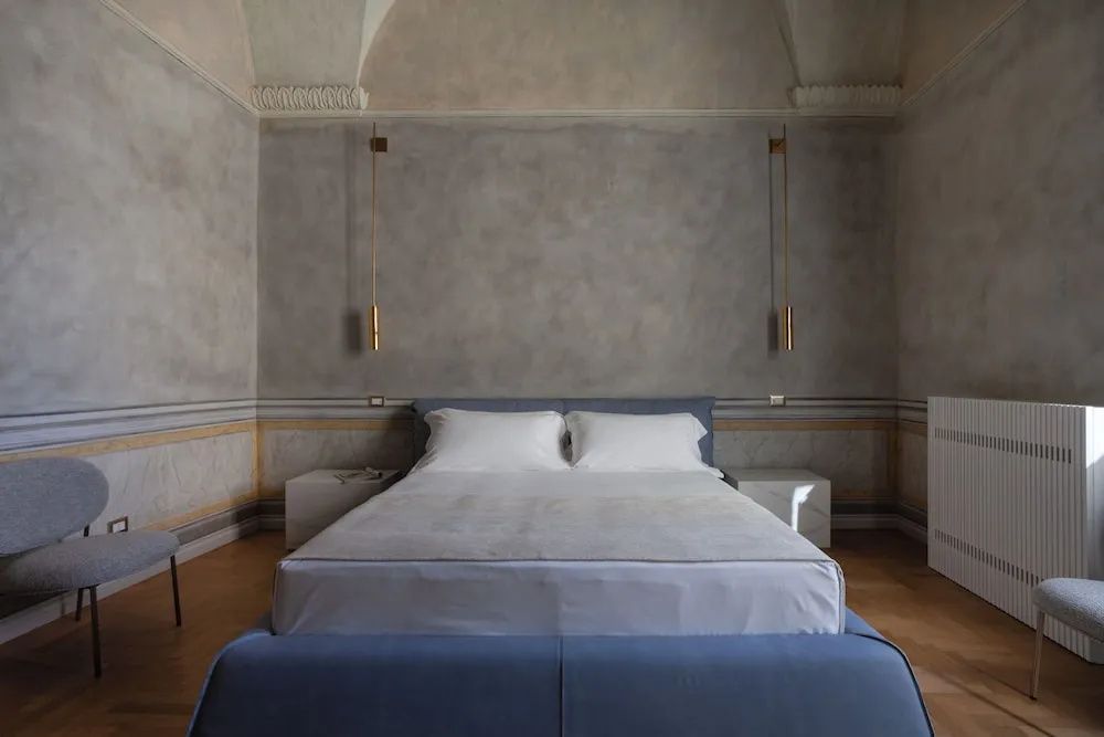 Doppelbett mit blauem Rahmen, Nachttischen und Hängeleuchten vor grauer Wand.