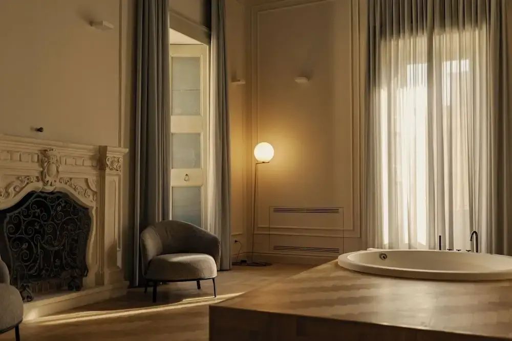 Geräumiges Zimmer mit Whirlpool, Sessel, Kamin und warmem Licht.