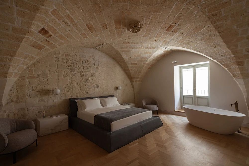 Doppelbett und Badewanne in einem Zimmer mit historischem Steingewölbe.