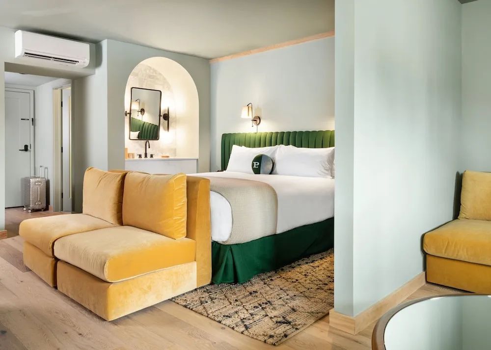 Hotelzimmer mit grünem Doppelbett, gelbem Samtsofa und Nische im Hintergrund.