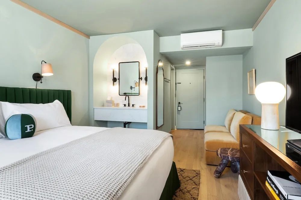 Hotelzimmer mit grünem Kopfteil, hellgrünen Wänden, offener Waschkoje und gelbem Sofa.