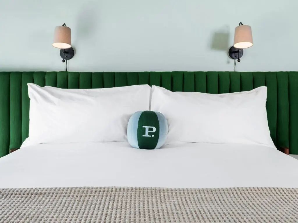Doppelbett mit weißer Bettwäsche, grünem Samtkopfteil und zwei Wandleuchten.