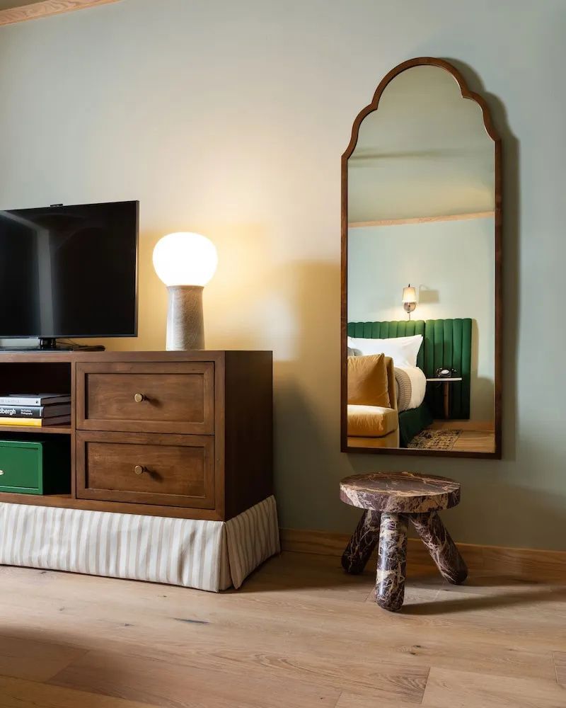 Holzschrank mit Fernseher, Tischleuchte und ein Wandspiegel mit einem Hocker.