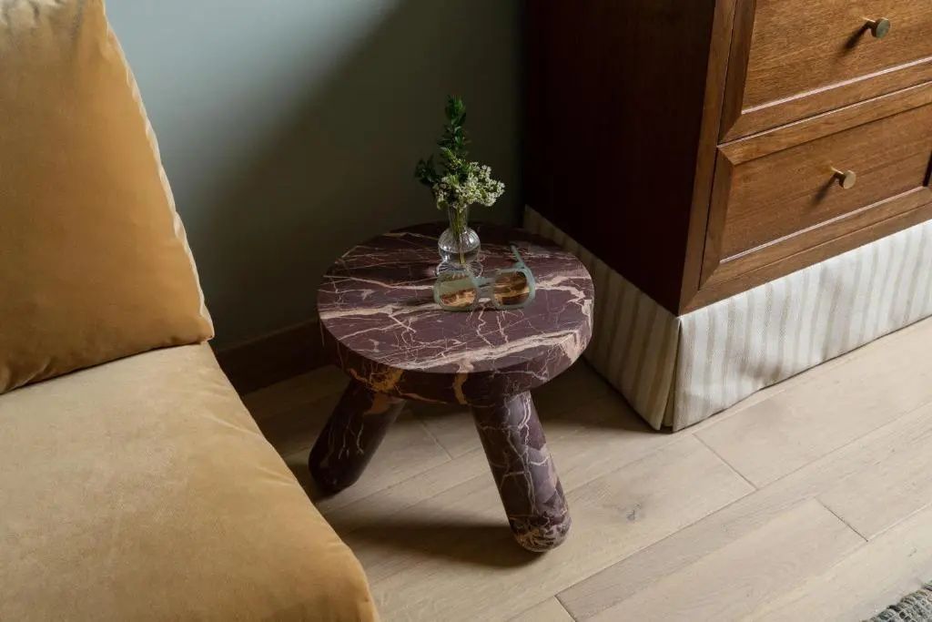 Marmorierter Beistelltisch mit Blumenvase neben einem samtigen Sofa.