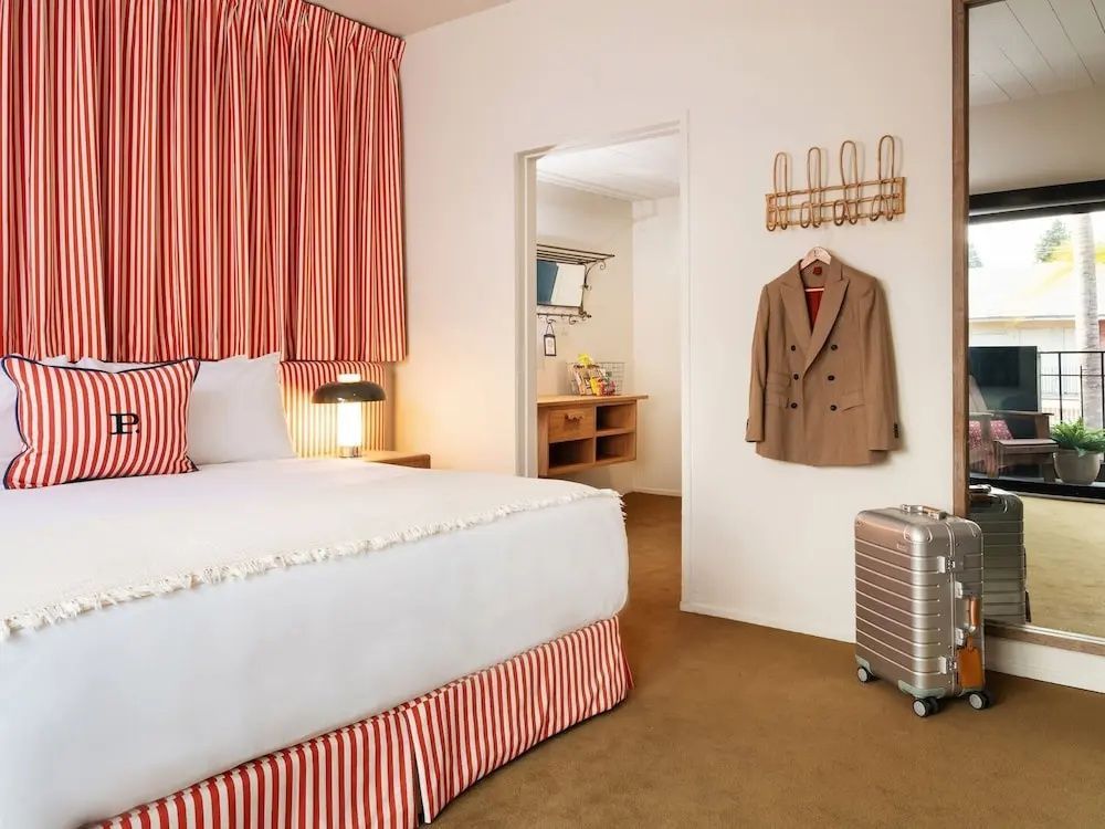 Doppelbett mit rot-weiß gestreiftem Kopfteil und Koffer im Hotelzimmer.