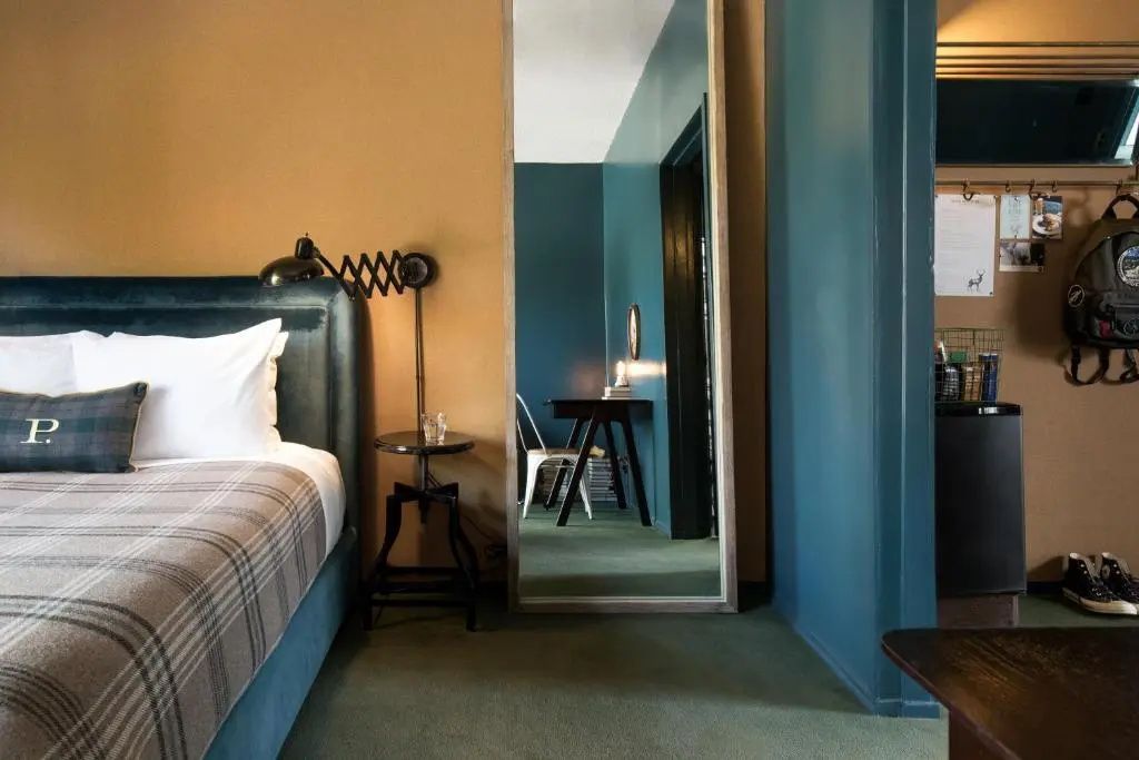 Hotelzimmer mit großem Ganzkörperspiegel, samtenem Kopfteil und verstellbarer Wandleuchte.