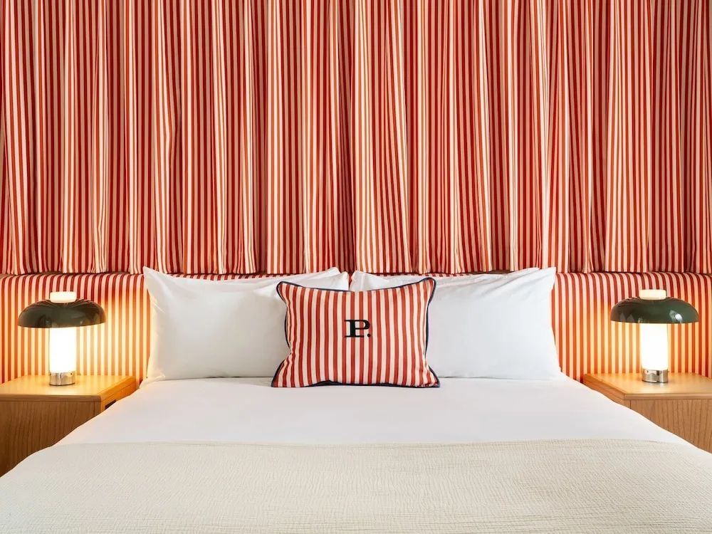 Doppelbett mit einem rot-weiß gestreiften Kissen und passendem Hintergrund.