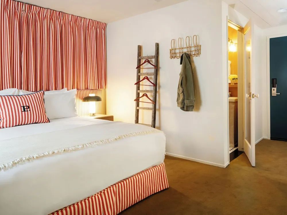 Hotelzimmer mit Doppelbett, hölzerner Deko-Leiter und Zugang zum Badezimmer.