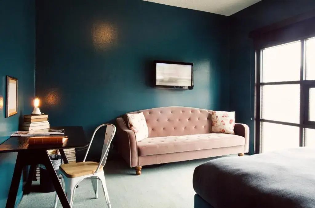 Wohnbereich eines Zimmers mit einem altrosa Polstersofa, Kissen, Stuhl und Fernseher an der Wand.