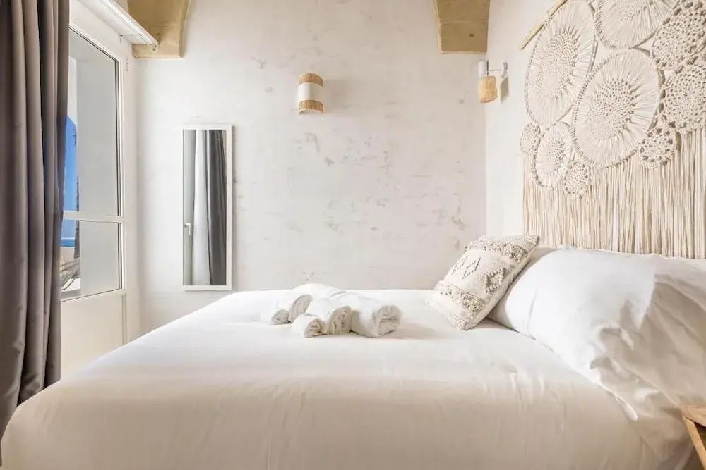 Hell eingerichtetes Schlafzimmer mit weißem Doppelbett und Wanddekoration.