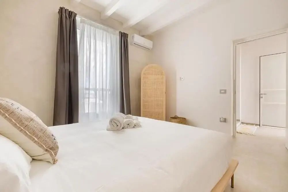 Helles Schlafzimmer mit weiß bezogenem Doppelbett, Vorhängen und Klimaanlage.