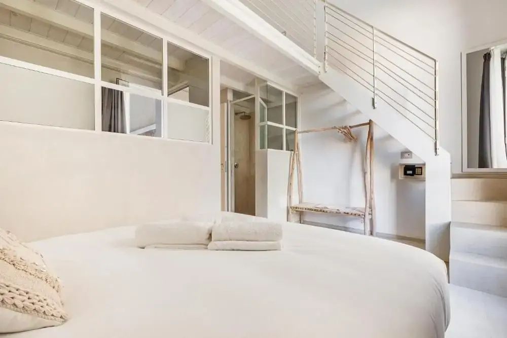 Weißes Doppelbett in einem Zimmer mit Treppe zu einer Galerieebene.