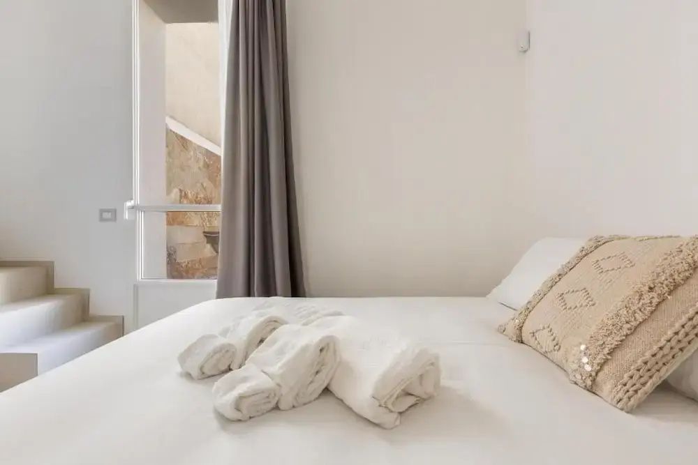 Doppelbett mit gefalteten Handtüchern vor einem bodentiefen Fenster.