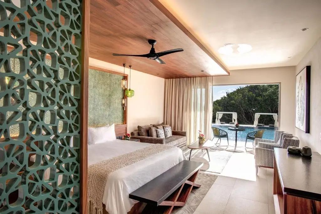 Hotelzimmer mit Doppelbett, Sofa und einer Glasfront mit Blick auf einen Pool.