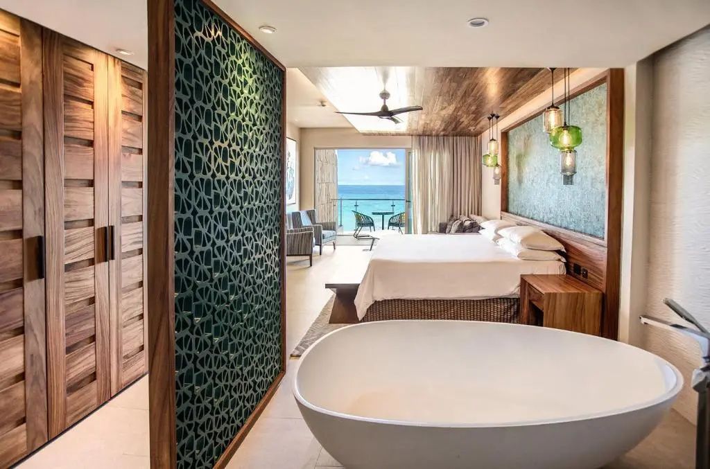 Hotelzimmer mit freistehender Badewanne, Doppelbett und Balkon mit Blick auf das blaue Meer.