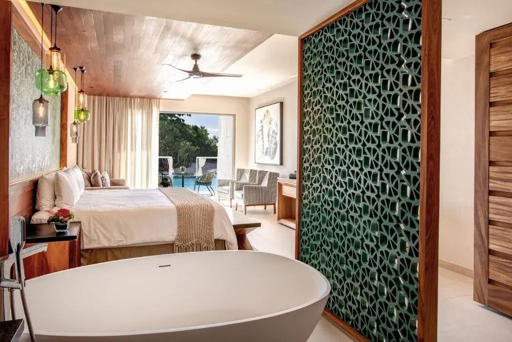 Zimmer mit freistehender Wanne, Doppelbett und Terrassenzugang zum Außenbereich.
