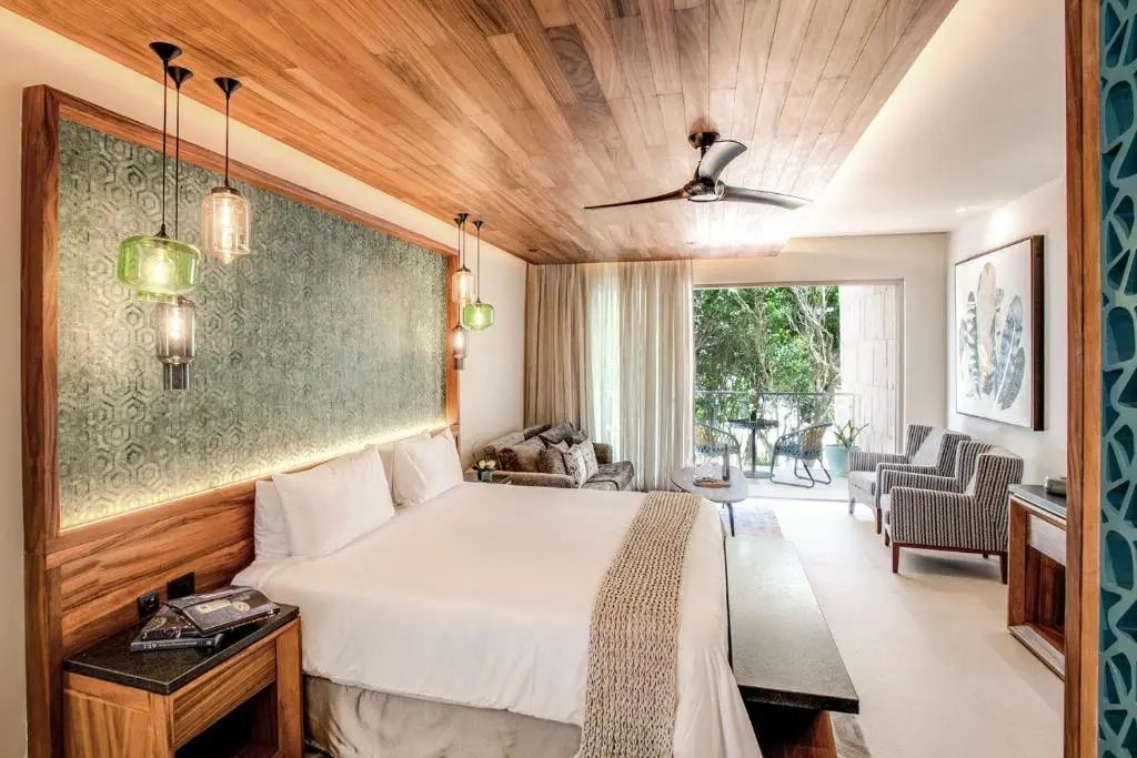 Hotelzimmer mit Doppelbett, Deckenventilator, Holzdecke und offenem Balkonbereich.