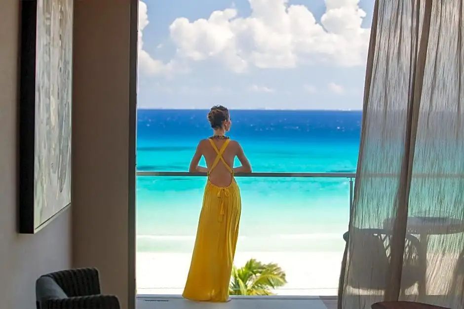 Blick von einer Terrasse auf den hellen Sandstrand und das türkisfarbene Wasser.