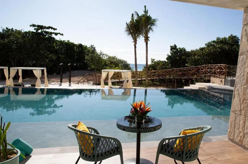 Sitzbereich auf einer Terrasse an einem Pool mit Blick auf Tropenpflanzen und Meer.