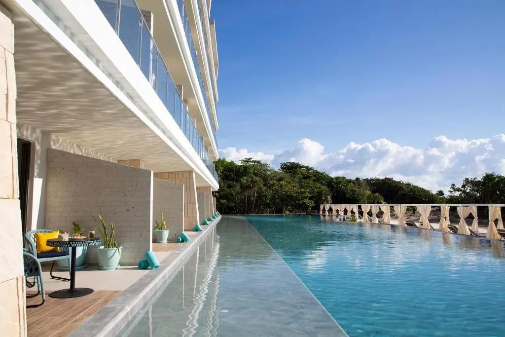 Langer Pool direkt vor der Hotelfassade mit angrenzender tropischer Vegetation.