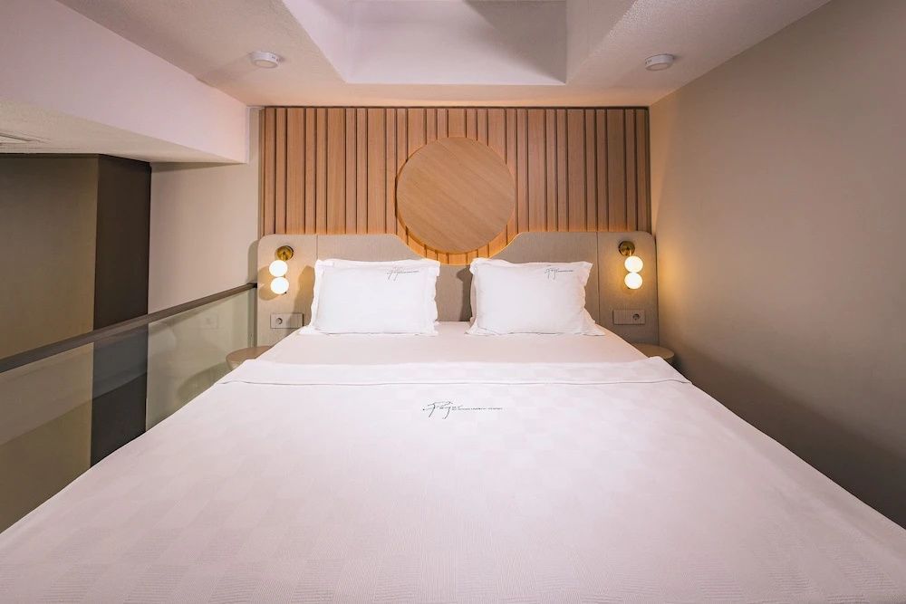 Doppelbett mit weißen Kissen und einer Wandverkleidung aus Holzlamellen.
