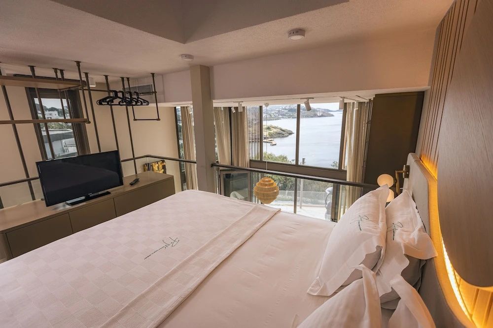 Doppelbett auf einer Galerie mit großem Fenster und Ausblick auf das Meer und die Küste.