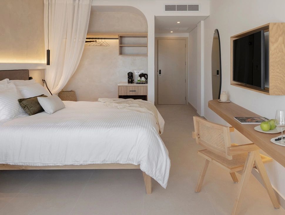 Hell eingerichtetes Hotelzimmer mit Doppelbett, Schreibtisch und Stuhl aus Holz.