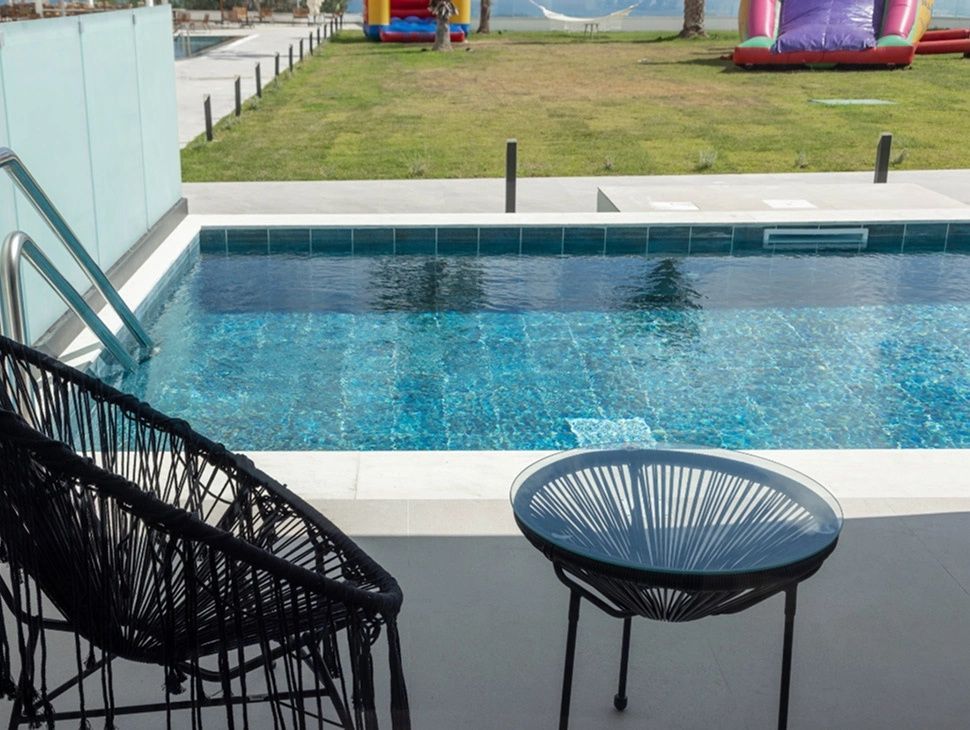 Privater Pool direkt an der Terrasse mit Sitzmöbeln im Vordergrund und Wiese im Hintergrund.
