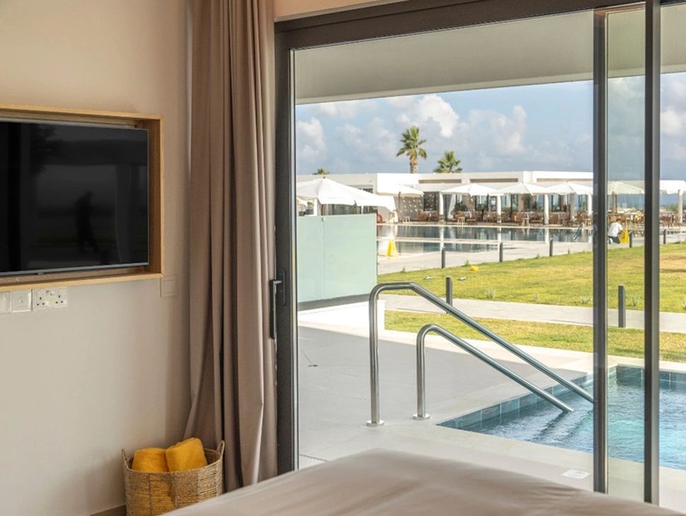 Blick durch ein großes Fenster aus dem Hotelzimmer auf einen privaten Pool und Palmen.