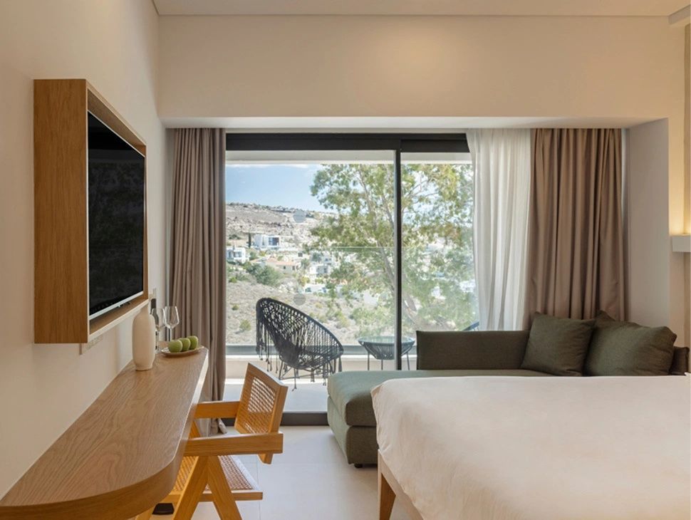 Modernes Hotelzimmer mit Schreibtisch, Sofa und Blick auf den Balkon und die Landschaft.