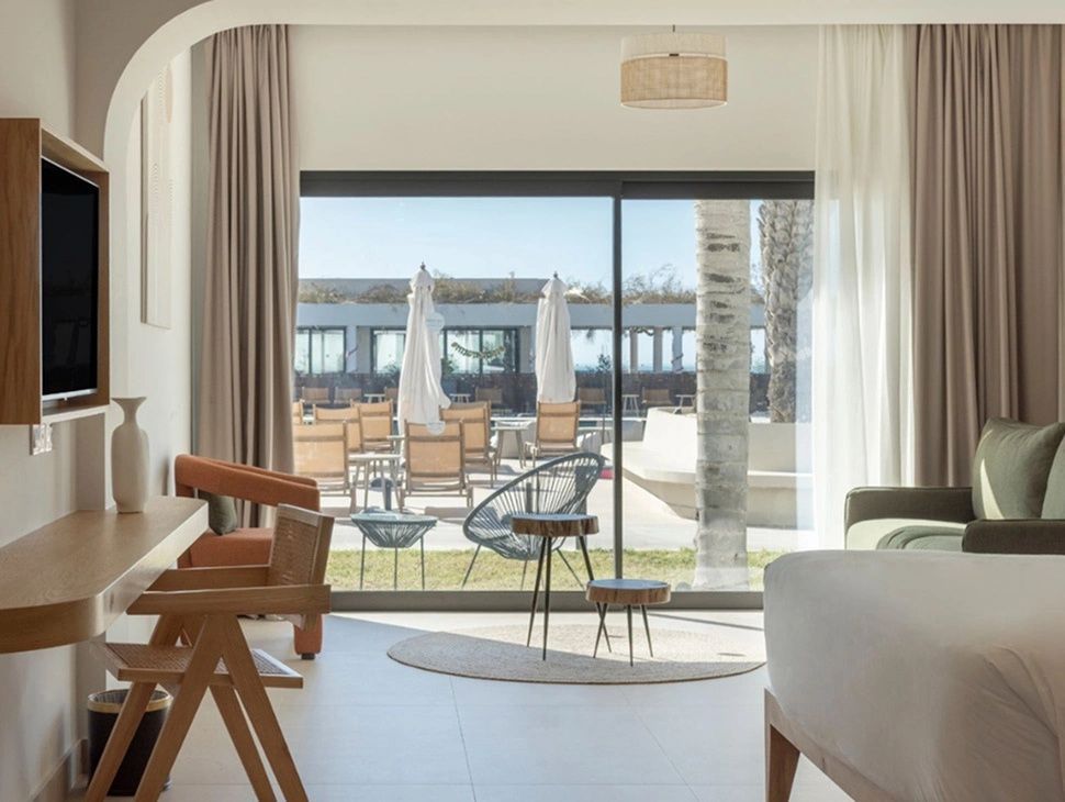 Zimmerinterieur mit Blick durch die Terrassentür auf den Außenbereich mit Liegestühlen.