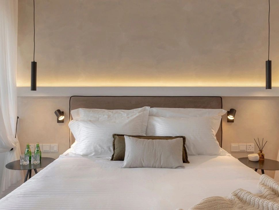 Gemachtes Doppelbett mit weißen Kissen, Leselampen und warmer Lichtleiste an der Wand.
