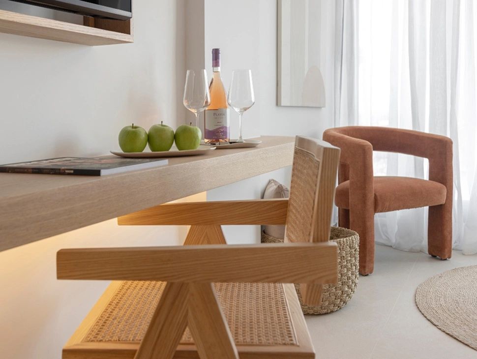 Holzablage mit einer Flasche Wein, Gläsern, grünen Äpfeln und Stühlen im Hotelzimmer.
