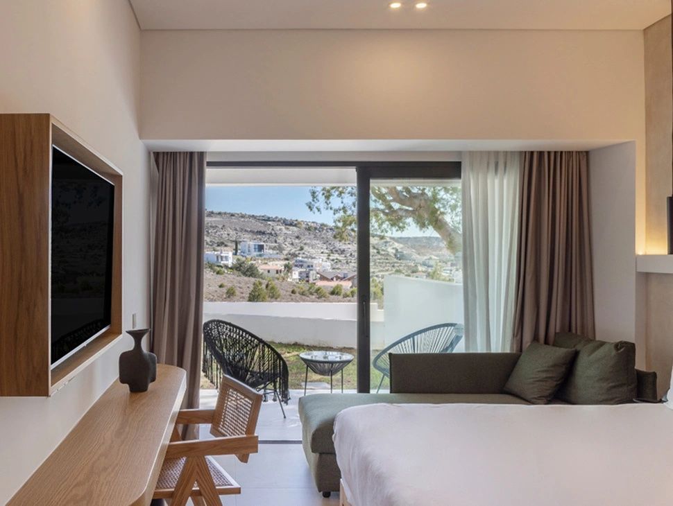 Hell eingerichtetes Hotelzimmer mit Doppelbett, Sitzbereich und Zugang zur eigenen Terrasse.