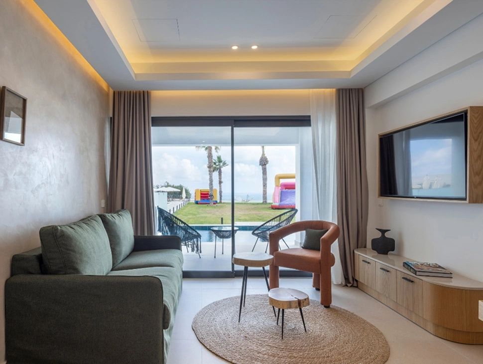 Wohnbereich einer Suite mit grünem Sofa, Couchtischen, Sessel und Blick auf den Poolbereich.