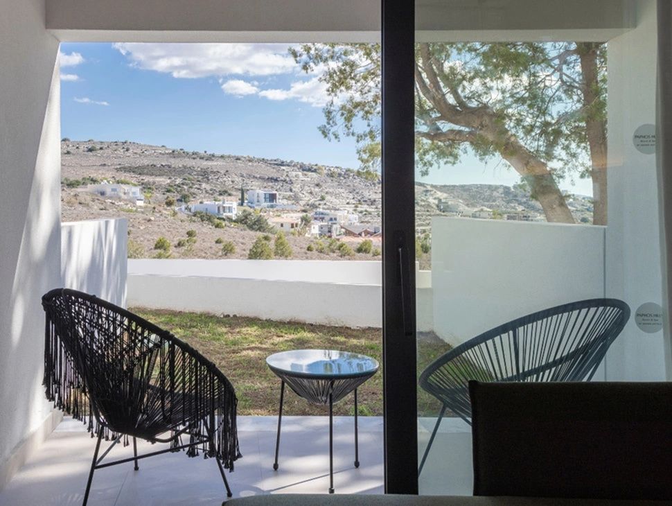 Blick durch eine Glastür auf eine Terrasse mit zwei Stühlen und Aussicht auf die hügelige Landschaft.