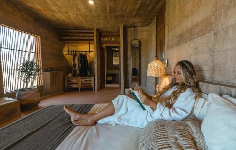 Frau liest ein Buch auf dem Bett in einem modern gestalteten Zimmer aus Sichtbeton.