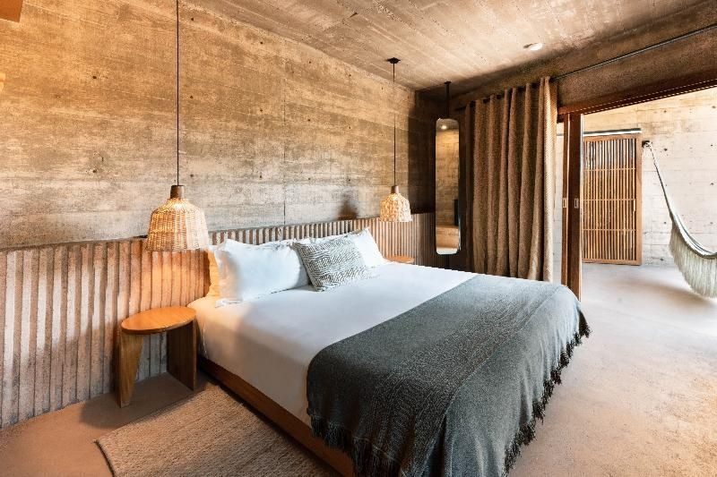 Doppelbett in einem Hotelzimmer mit Betonwänden und Lampen aus Naturmaterialien.