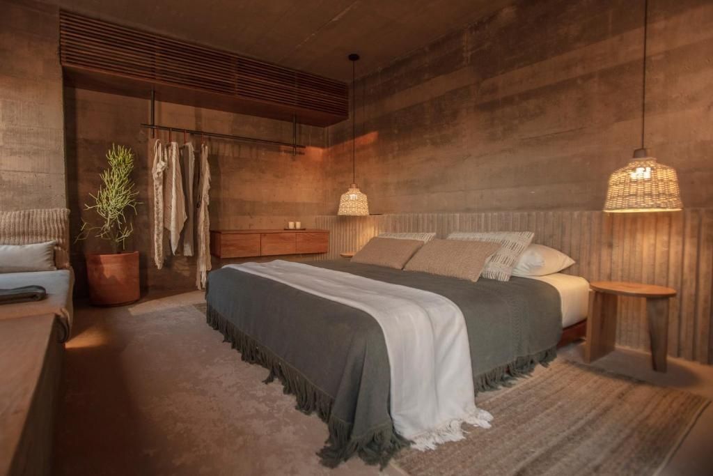 Hotelzimmer mit großem Doppelbett, dunkler Tagesdecke und offenen Wänden aus Stampfbeton.