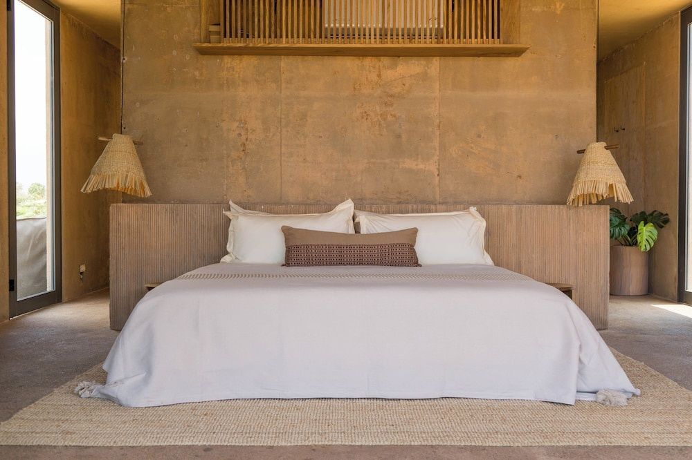 Doppelbett mit weißer Bettwäsche, Kissen und Erdtönen an der Wand im Hotelzimmer.