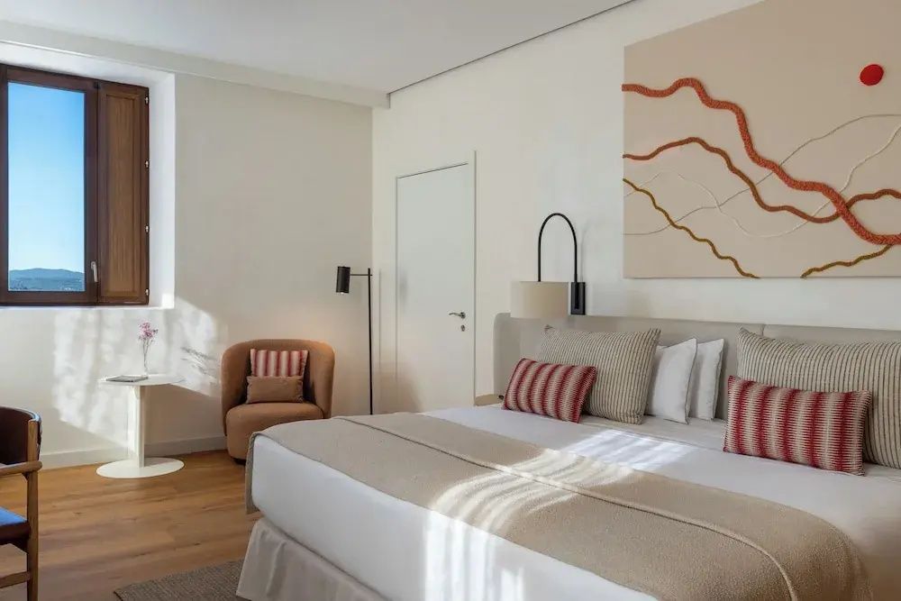Doppelbett mit gestreiften Kissen, Kunstwerk an der Wand und einem Sessel im Hintergrund.