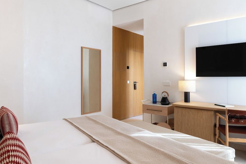Blick durch das Hotelzimmer in Richtung Holztür, Schreibtisch und Wandfernseher.