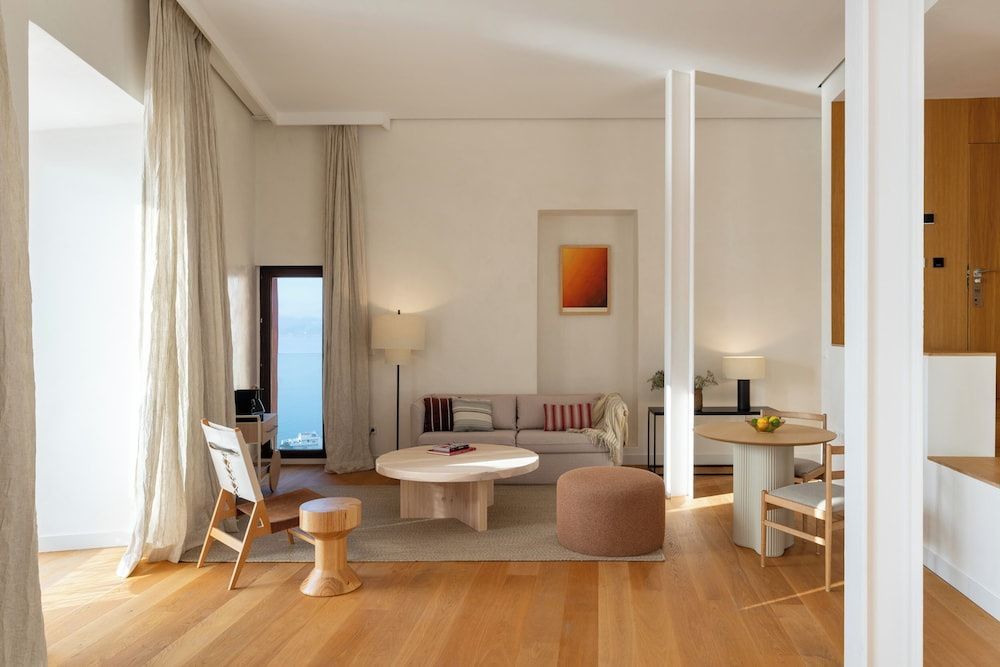 Geräumiger Wohnbereich einer Suite mit Sofa, Holztischen, Stühlen und Ausblick auf das Meer.