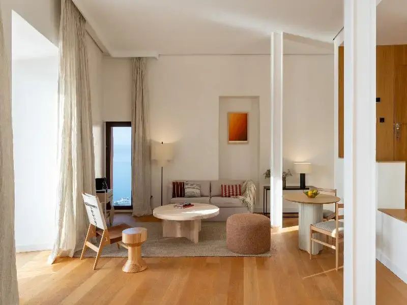 Geräumiger Wohnbereich mit Holzboden, einem Sofa, verschiedenen Sitzmöbeln und Fenster zum Meer.