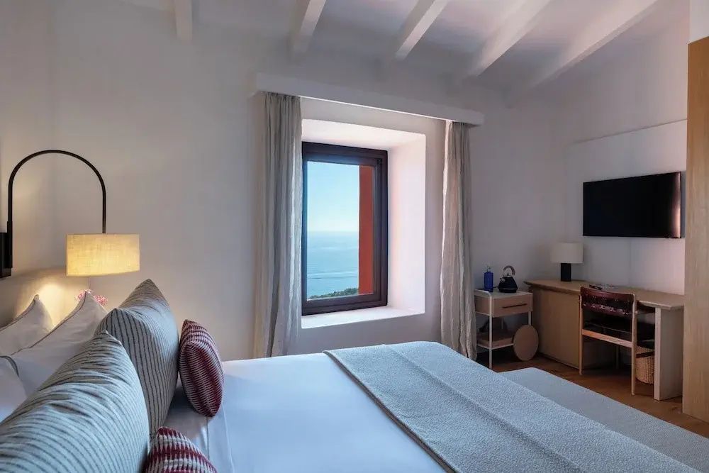 Schlafzimmer mit einem Doppelbett, Parkettboden und Blick aus dem Fenster auf das Meer.