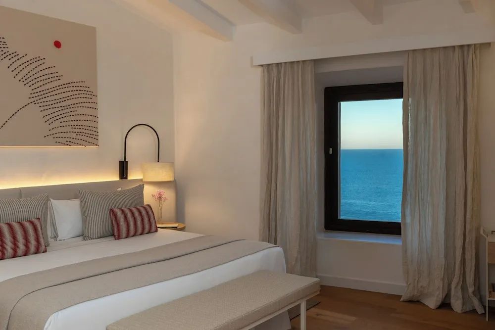 Helles Hotelzimmer mit Doppelbett und Fenster mit Blick auf das blaue Meer.